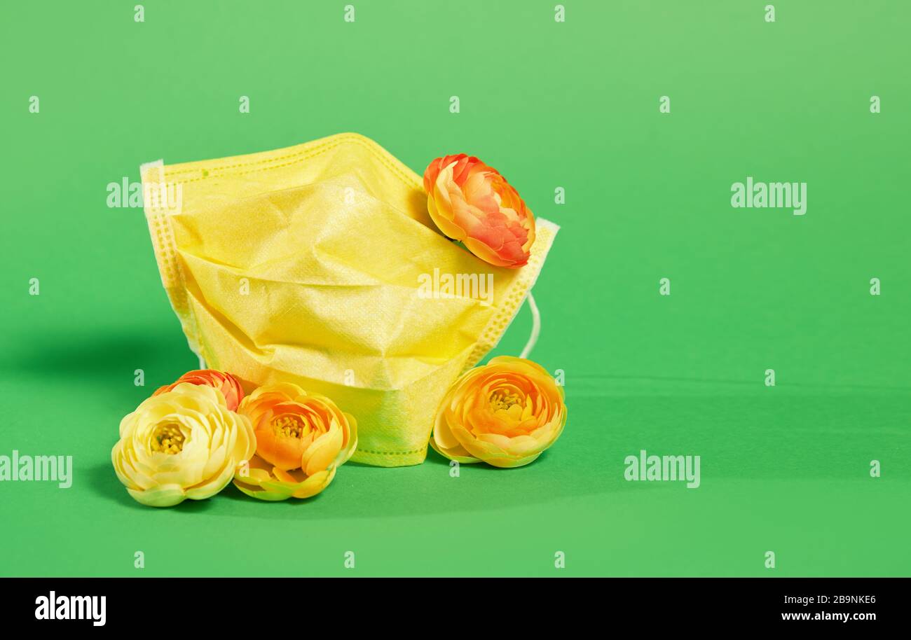 Maschera medica protettiva gialla con fiori freschi su sfondo verde. Tendenza della stagione dei virus e della quarantena Foto Stock