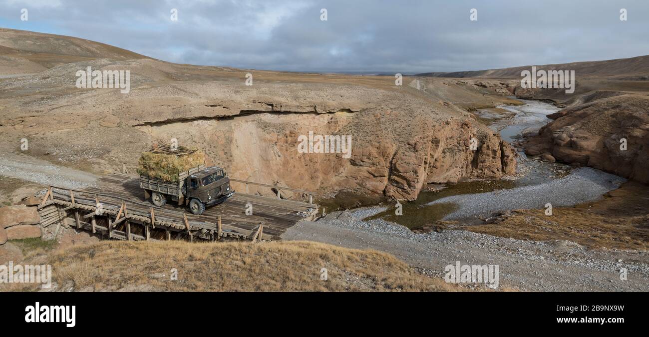 Un camion sovietico GAZ-66 4x4 ben caricato con balle di paglia di fieno che attraversano una brigata di legno su un piccolo canyon nella valle di Ak-sai che si dirige verso il Kol Suu lak Foto Stock