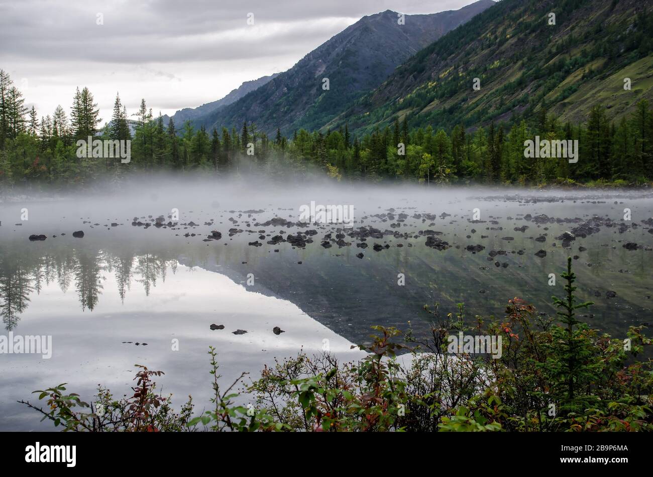 Sulla riva di un lago di montagna, pietre e foresta. giorno nuvoloso, luce naturale Foto Stock