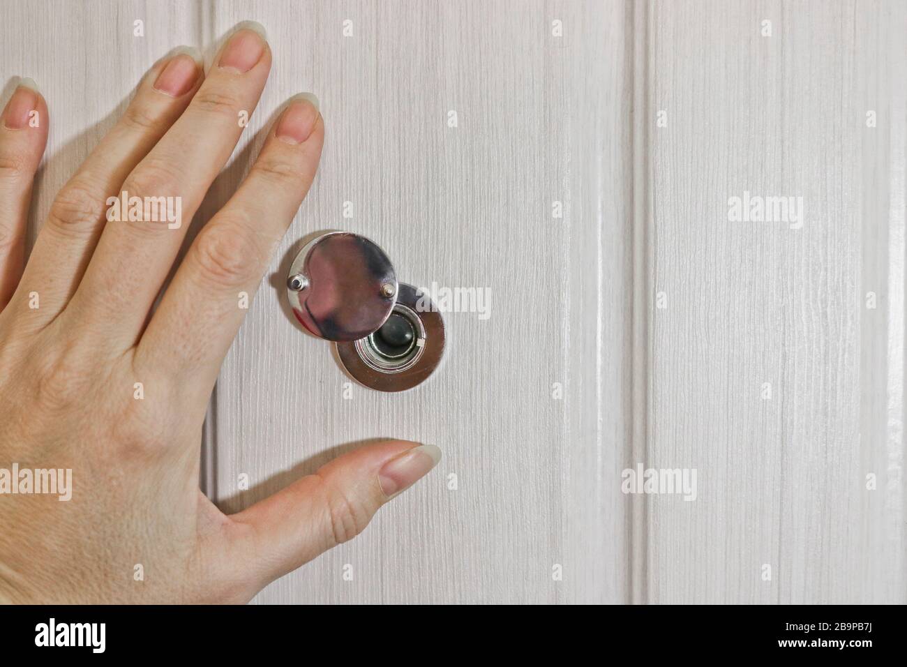 Una mano femmina apre la serranda sul peephole della porta anteriore. Il concetto di sicurezza e cautela. Foto Stock