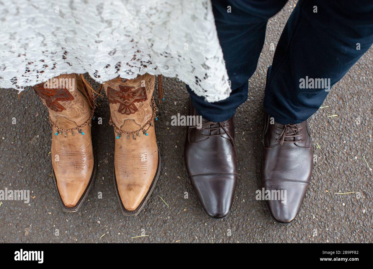 Sposa alternativa e sposo il giorno del matrimonio indossando stivali cowboy Foto Stock