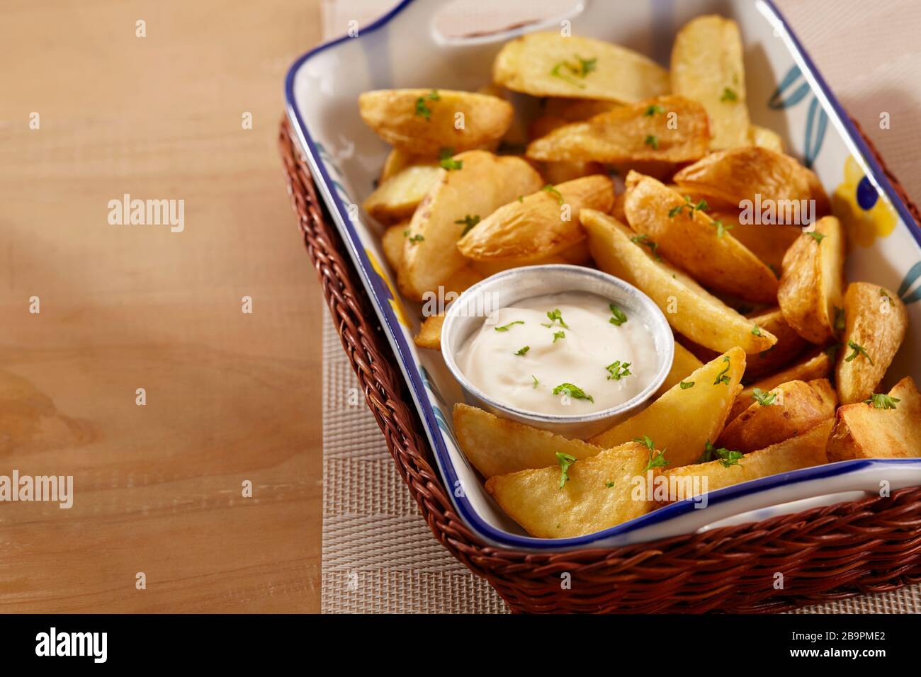 Una porzione di zeppe di patate viene servita in un vassoio di rattan con salsa maionese e una spolverata di foglie di prezzemolo Foto Stock