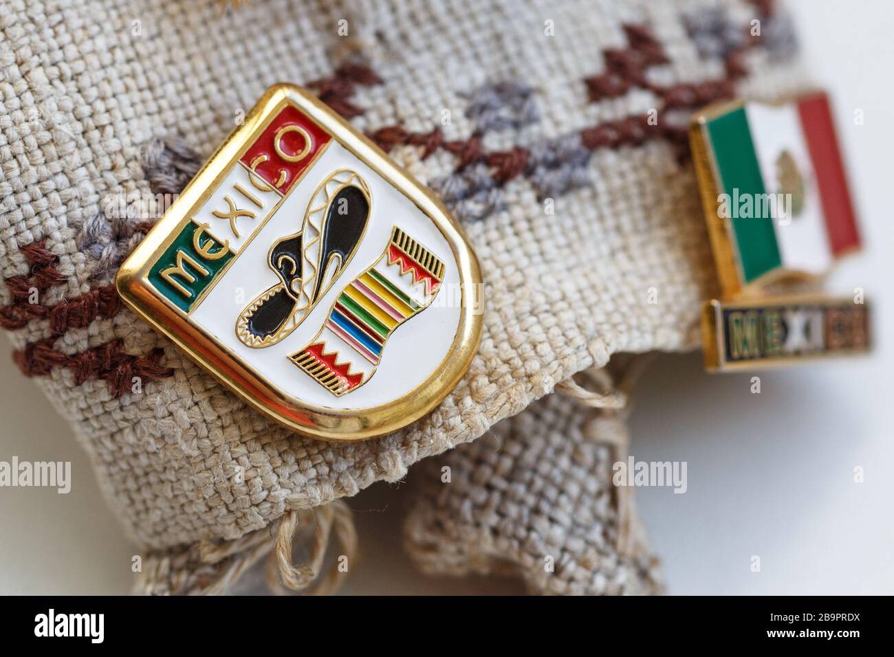 Distintivo di metallo con bandiera messicana, parola MESSICO, sombrero e poncho su di esso, messo su uno sfondo di lino Foto Stock