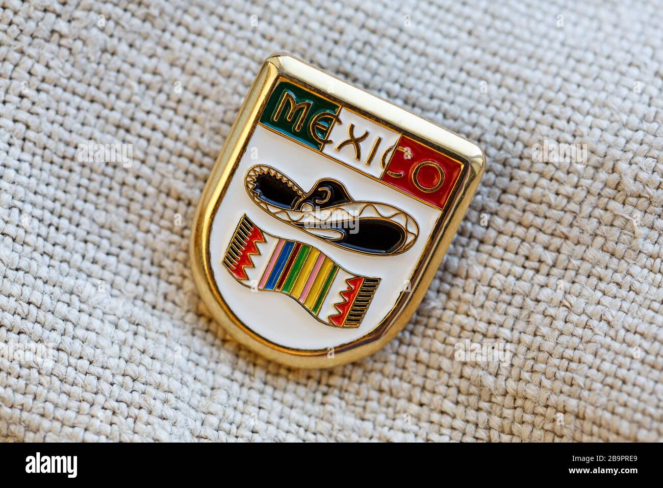 Distintivo di metallo con bandiera messicana, parola MESSICO, sombrero e poncho su di esso, messo su uno sfondo di lino Foto Stock