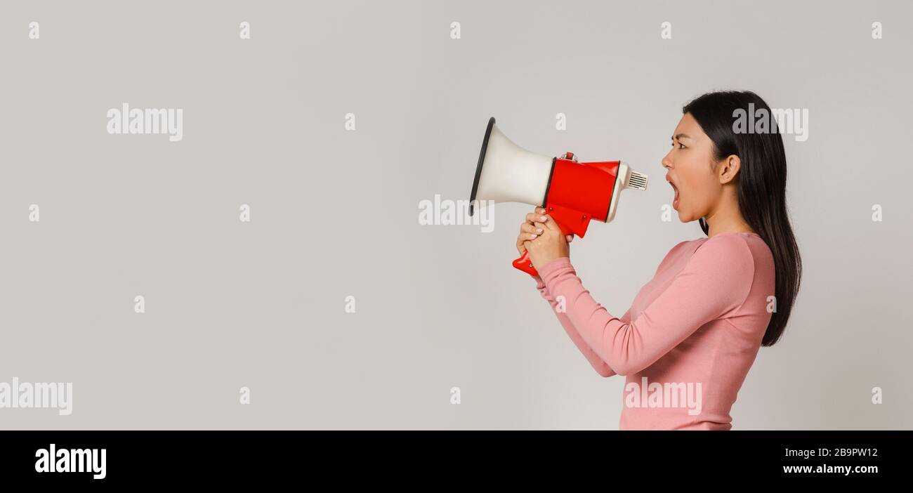 Emotiva donna asiatica che gridava in megaphone su sfondo grigio Foto Stock