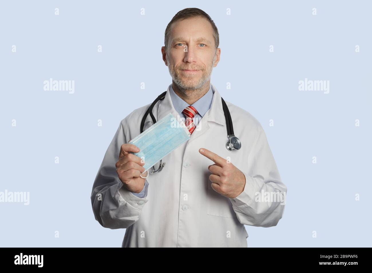 Un medico in un cappotto medico e uno stetoscopio sulle spalle mostra una maschera medica Foto Stock