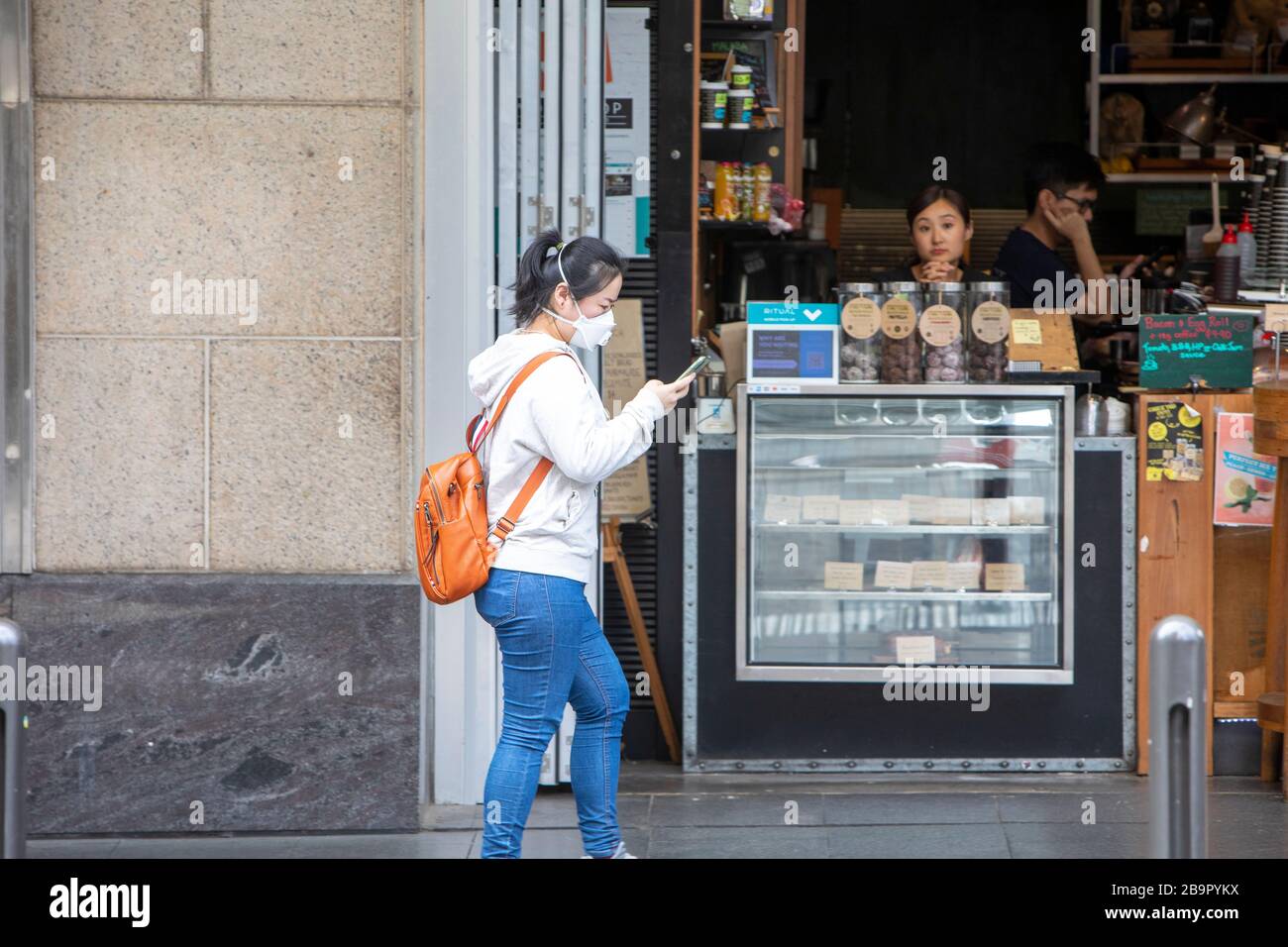 Centro di Sydney, Australia. Mercoledì 25 Marzo 2020..la signora asiatica che indossa la maschera cammina oltre i disprezzati proprietari di caffè nel centro della città di Sydney. Credit Martin Berry/Alamy Live News Foto Stock