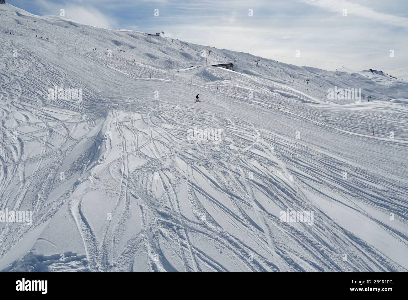 Sci con sciatore solitario nel mezzo. La pendenza è segnata da tracce irregolari di sci. Foto Stock