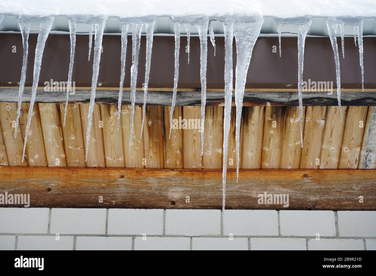Una lunga fila di sicli che si fondono da vicino appesi al tetto in legno annunciando la fine dell'inverno e la prossima primavera o il tempo di scongelamento come un simbolo Foto Stock