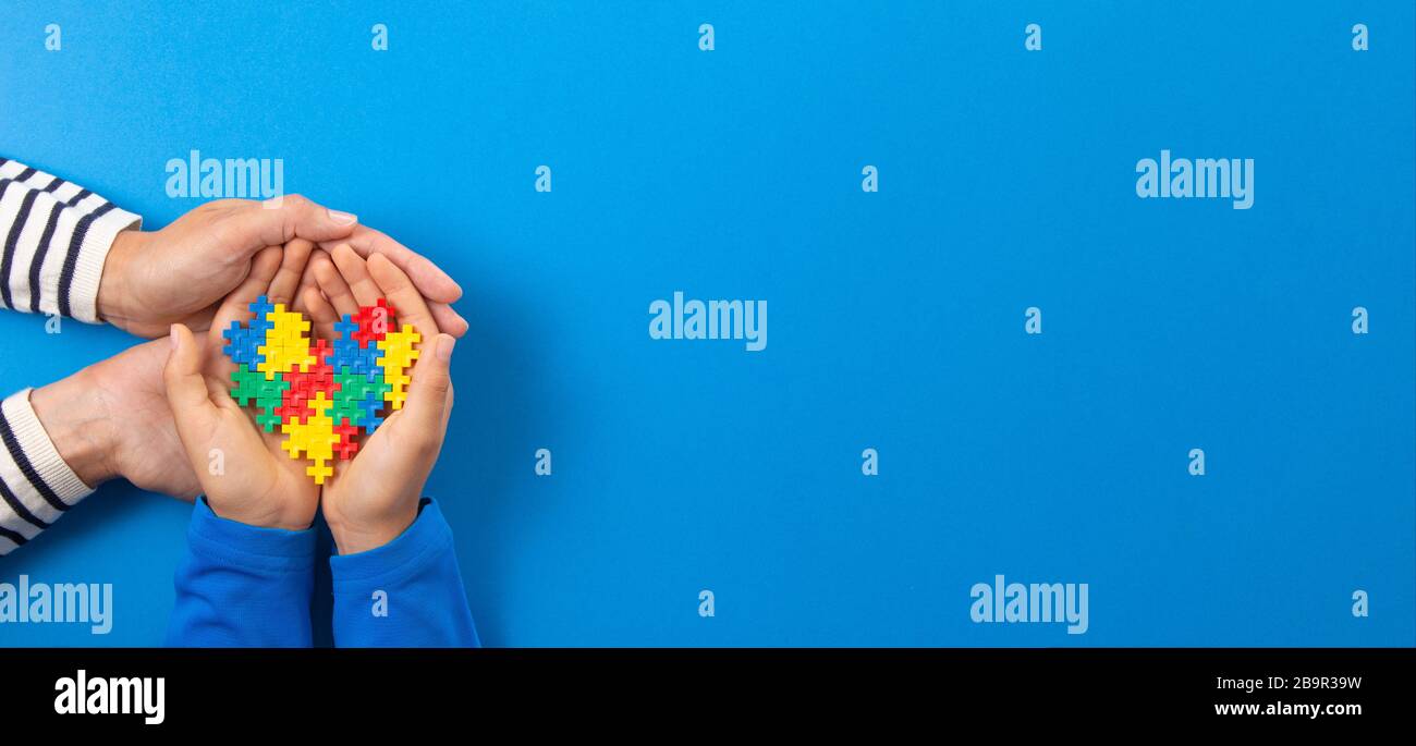 Concetto del giorno di consapevolezza di autismo del mondo. Mani per adulti e bambini che tengono il cuore del puzzle su sfondo blu chiaro Foto Stock