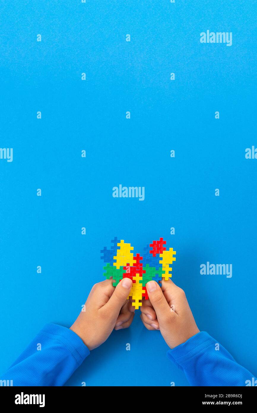Concetto del giorno di consapevolezza di autismo del mondo. Le mani del bambino tengono il cuore colorato del puzzle su sfondo blu Foto Stock