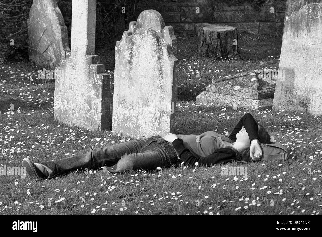 Morte e Maiden: Una ragazza addormentato tra le margherite in un cimitero: Il cimitero di Santa Caterina, Ventnor, Isola di Wight, Inghilterra, Regno Unito. Versione in bianco e nero. MODELLO RILASCIATO Foto Stock