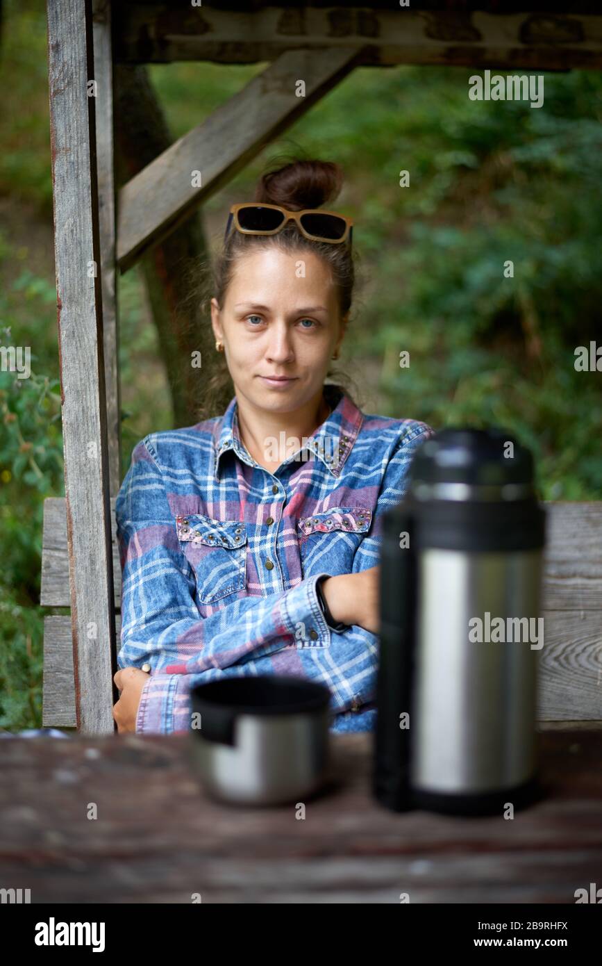 Giovane turista isesplorando nuovi luoghi e godendo il paesaggio naturale della foresta. Ragazza che ha riposo con bevanda calda, tè da thermos seduta sul legno Foto Stock