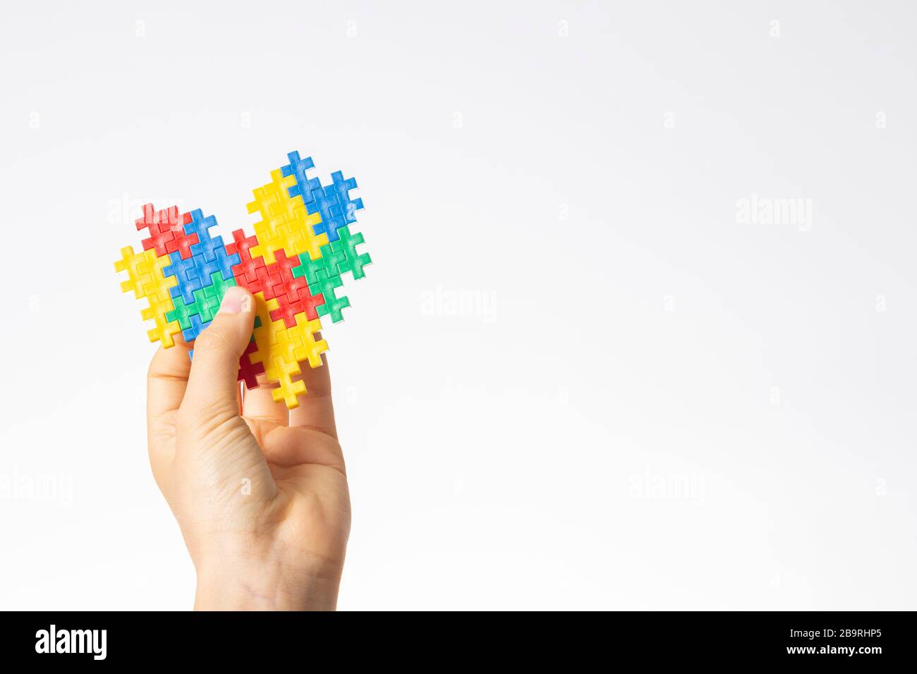 Concetto del giorno di consapevolezza di autismo del mondo. Le mani del bambino tengono il cuore colorato del puzzle su sfondo bianco Foto Stock