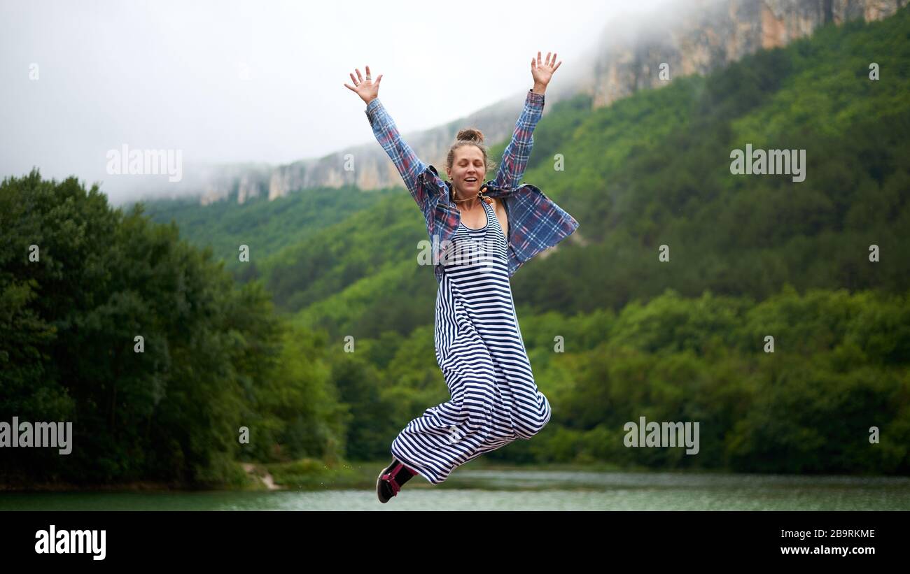 Donna informale vestita da trekking sotto la pioggia che balla vicino al lago in montagna. Espressione sincera e sincera. Foto Stock