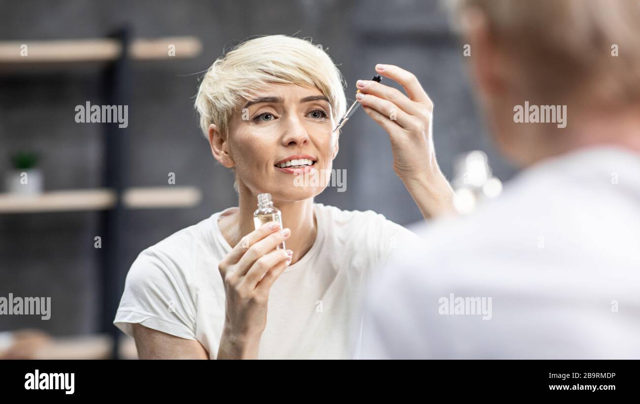 Donna che applica olio cosmetico cura della pelle in bagno, Panorama Foto Stock