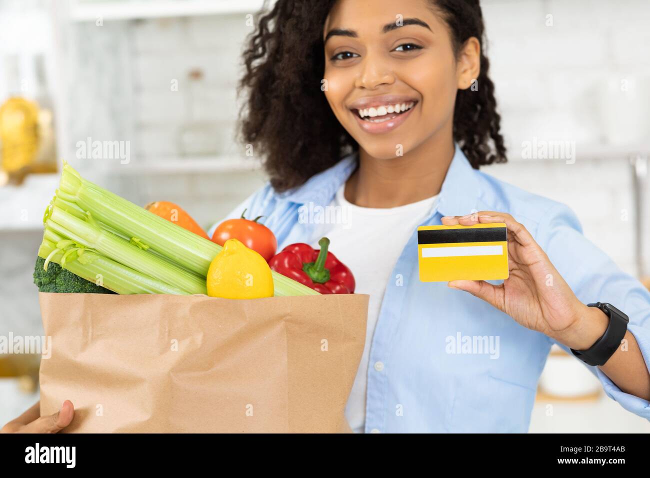 Afro ragazza che mostra carta di credito e sacchetto di carta con cibo Foto Stock