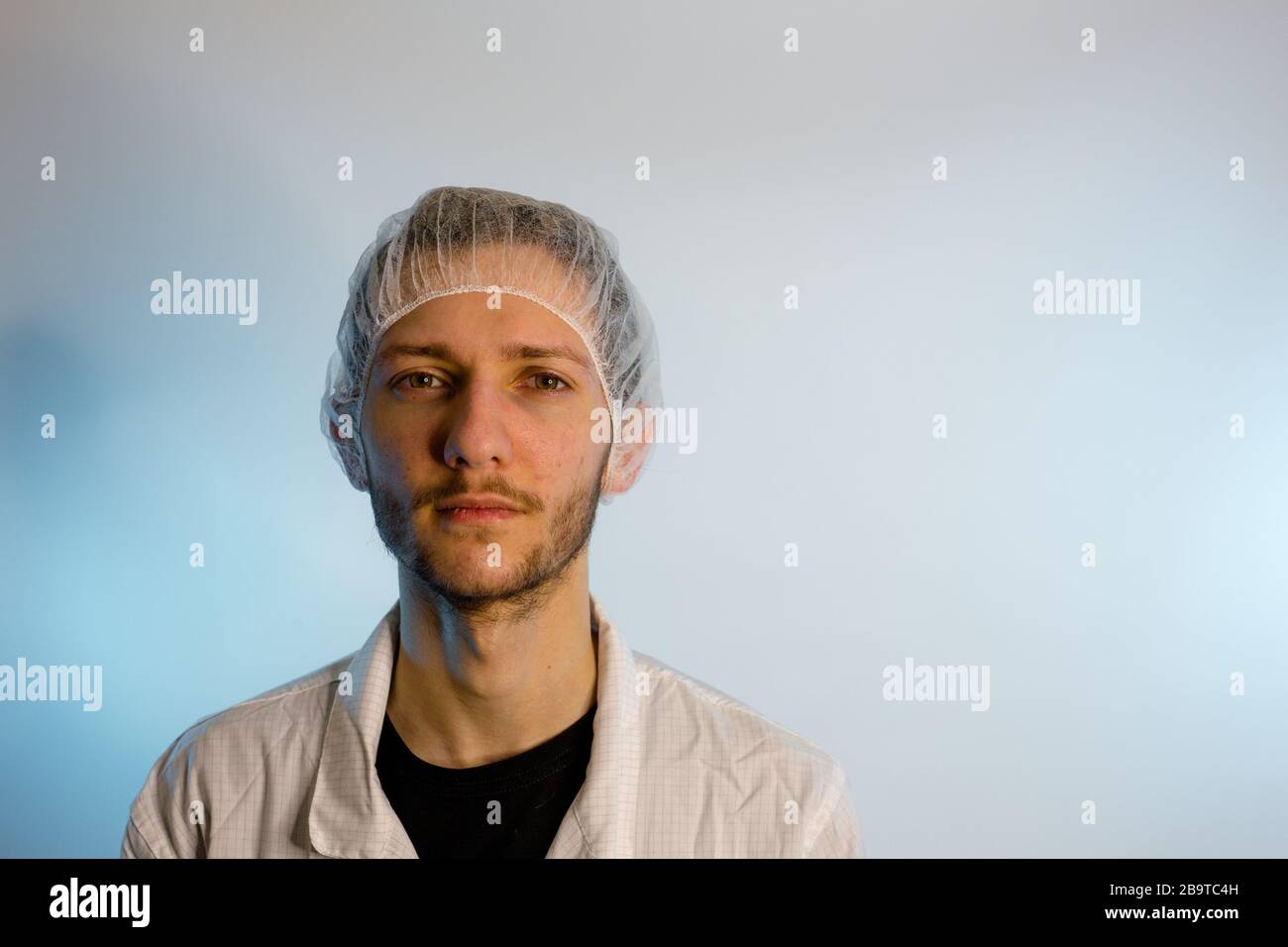 Un maschio adulto vestito in un camice bianco da laboratorio con una rete di capelli su. Pronto per lavorare in una camera bianca o in un laboratorio Foto Stock