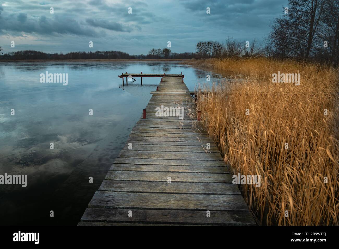 Un lungo ponte in legno e canneto sul lago e nuvole scure sul cielo Foto Stock