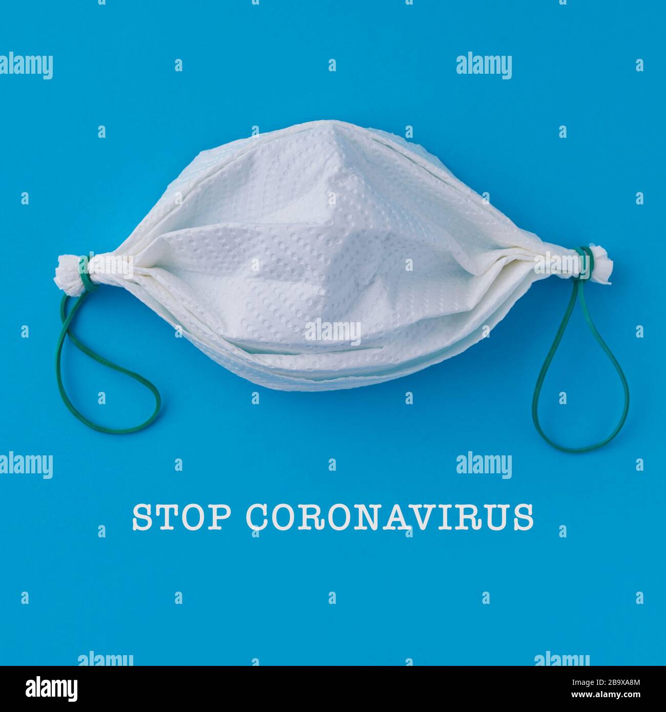 il testo stop coronavirus e una maschera facciale fatta in casa, fatta con carta asciugamano e bande di gomma, su uno sfondo blu Foto Stock