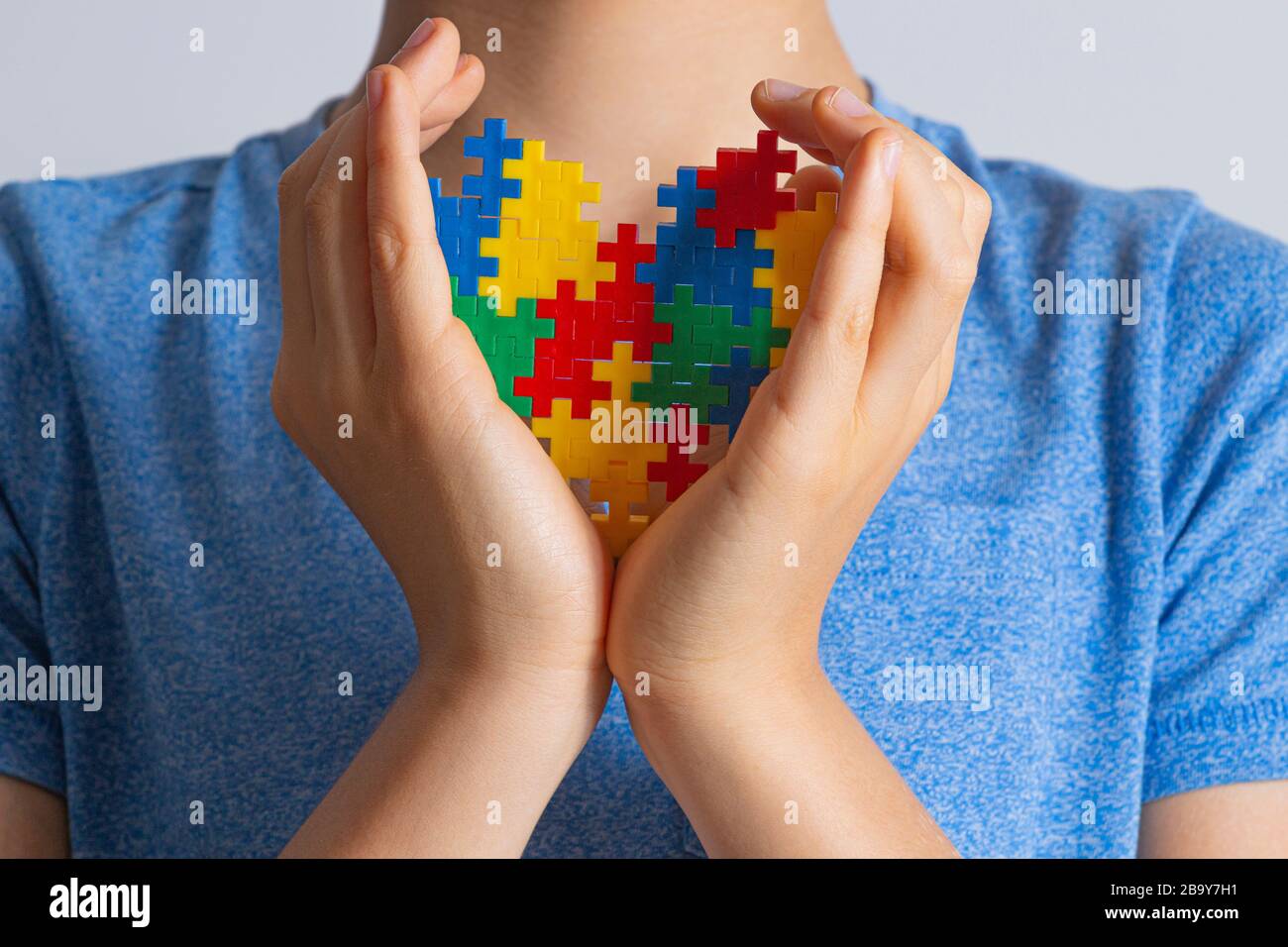 Concetto del giorno di consapevolezza di autismo del mondo. Le mani del bambino tengono il cuore colorato del puzzle contro di lui Foto Stock