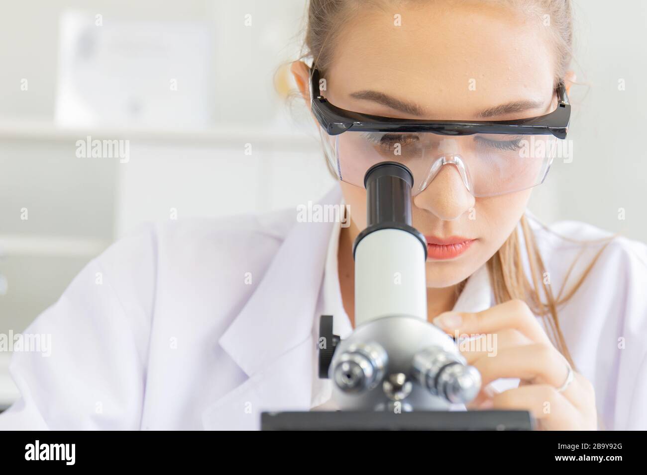 Belle scienziati femminili stanno guardando i microscopi in un laboratorio di scienza con varie attrezzature in laboratorio. Foto Stock