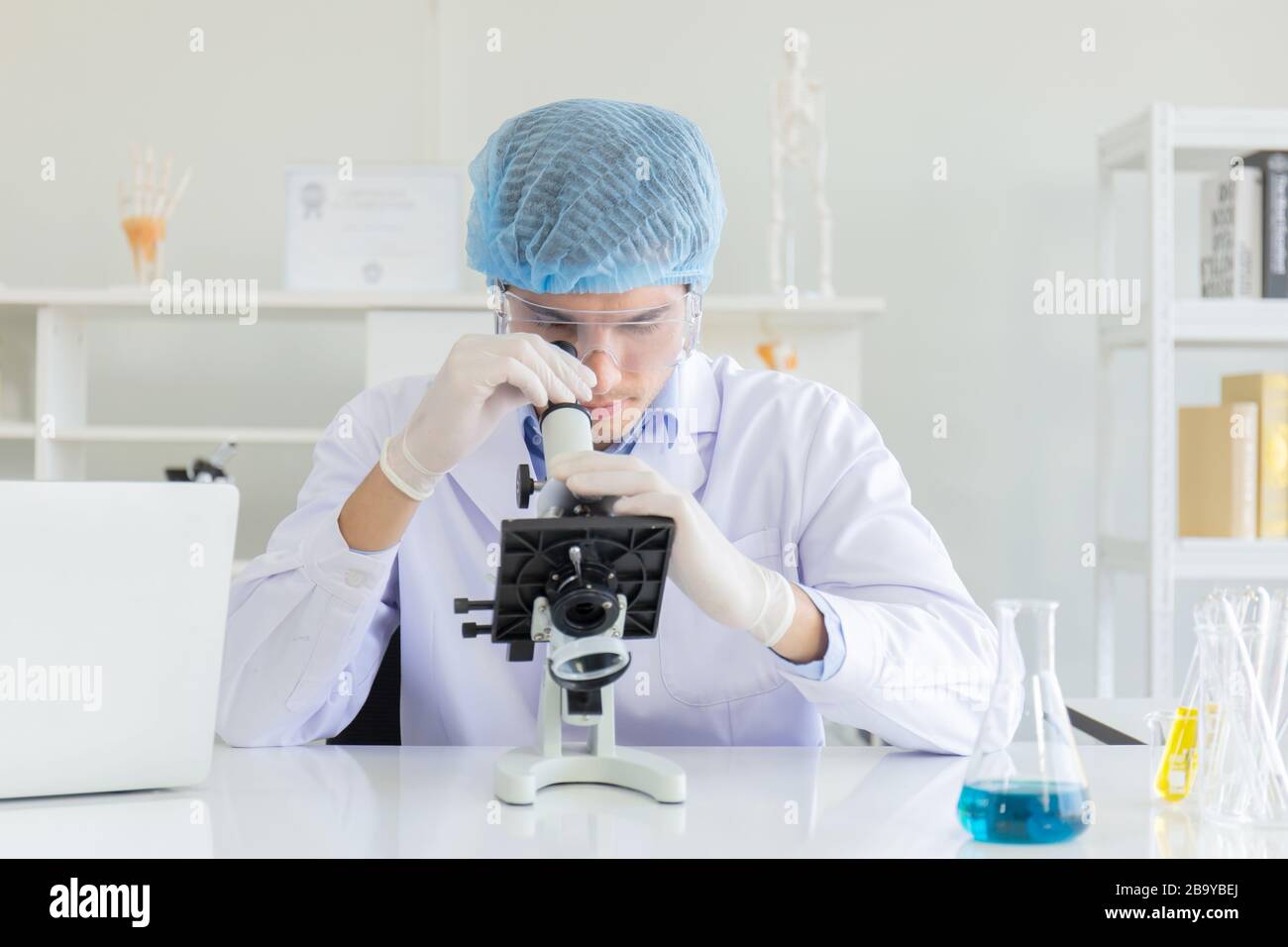 Giovane scienziato che usa il microscopio in laboratorio. Ricercatore  maschio che indossa un camice bianco seduto alla scrivania e che guarda i  campioni utilizzando il microscopio in laboratorio Foto stock - Alamy