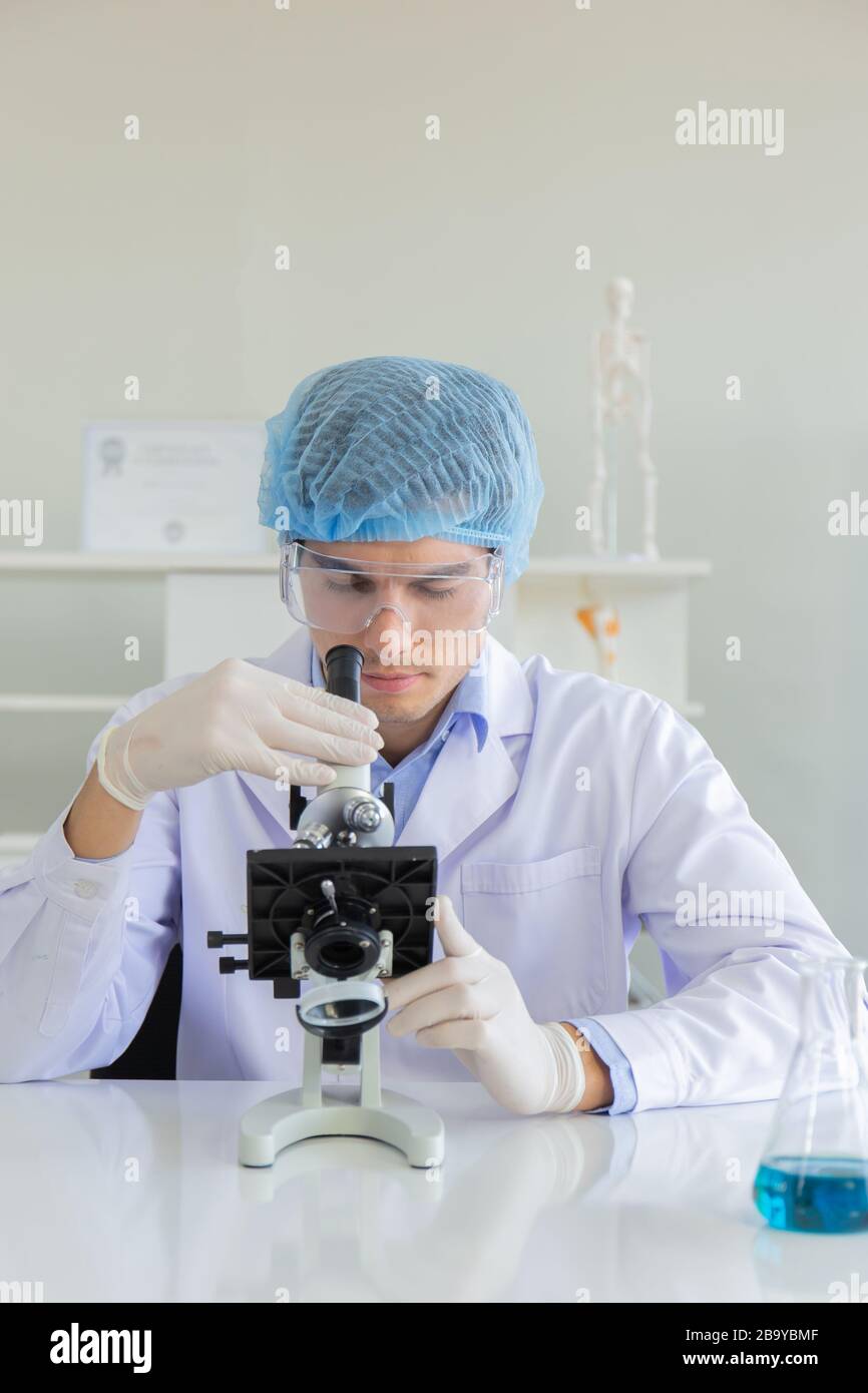 Giovane scienziato che usa il microscopio in laboratorio. Ricercatore  maschio che indossa un camice bianco seduto alla scrivania e che guarda i  campioni utilizzando il microscopio in laboratorio Foto stock - Alamy