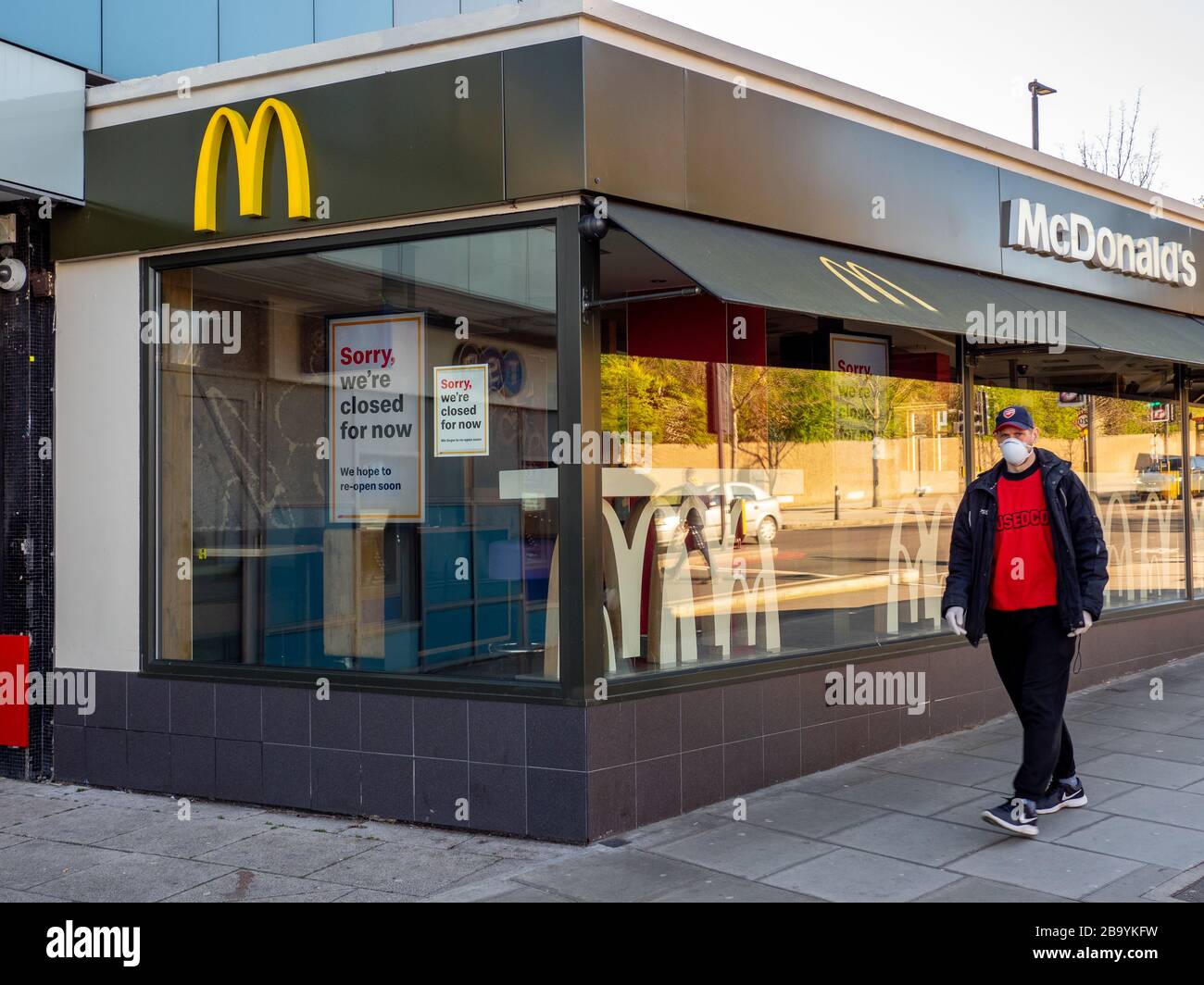 Un uomo che indossa una maschera e guanti passa davanti a un ristorante McDonald's che è chiuso a causa dell'epidemia di coronavirus. Foto Stock