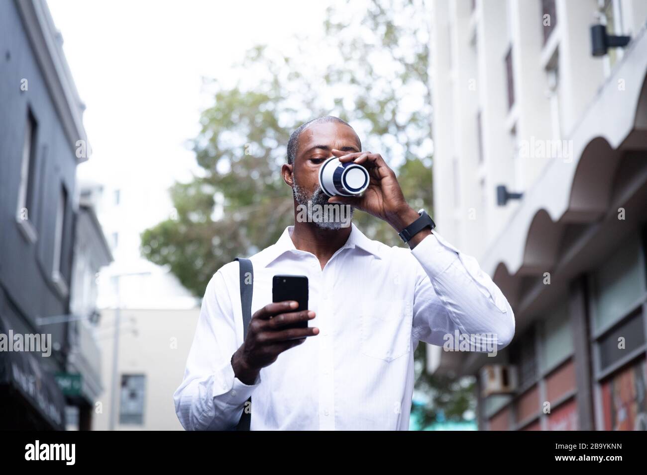 African American uomo bere caffè da asporto e utilizzando il suo telefono Foto Stock