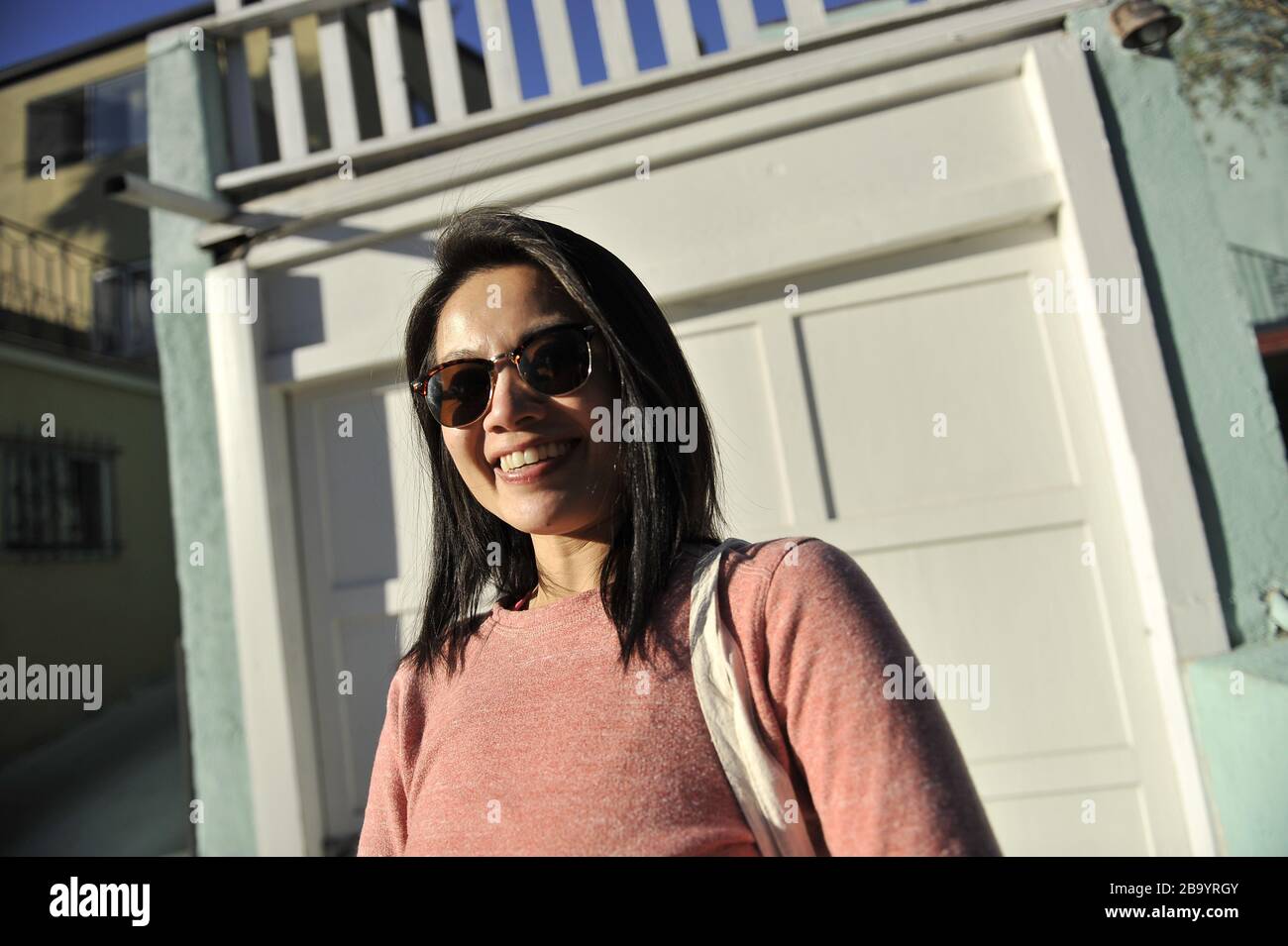 Donna asiatica in maglione rosa e occhiali da sole sorridenti candida  all'esterno Foto stock - Alamy