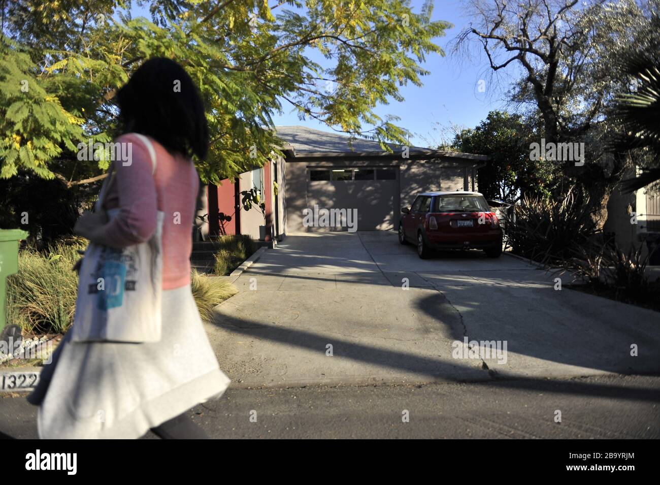 Donna asiatica che indossa un pullover rosa che cammina lungo un vialetto con una borsa tote intorno alle spalle. Foto Stock