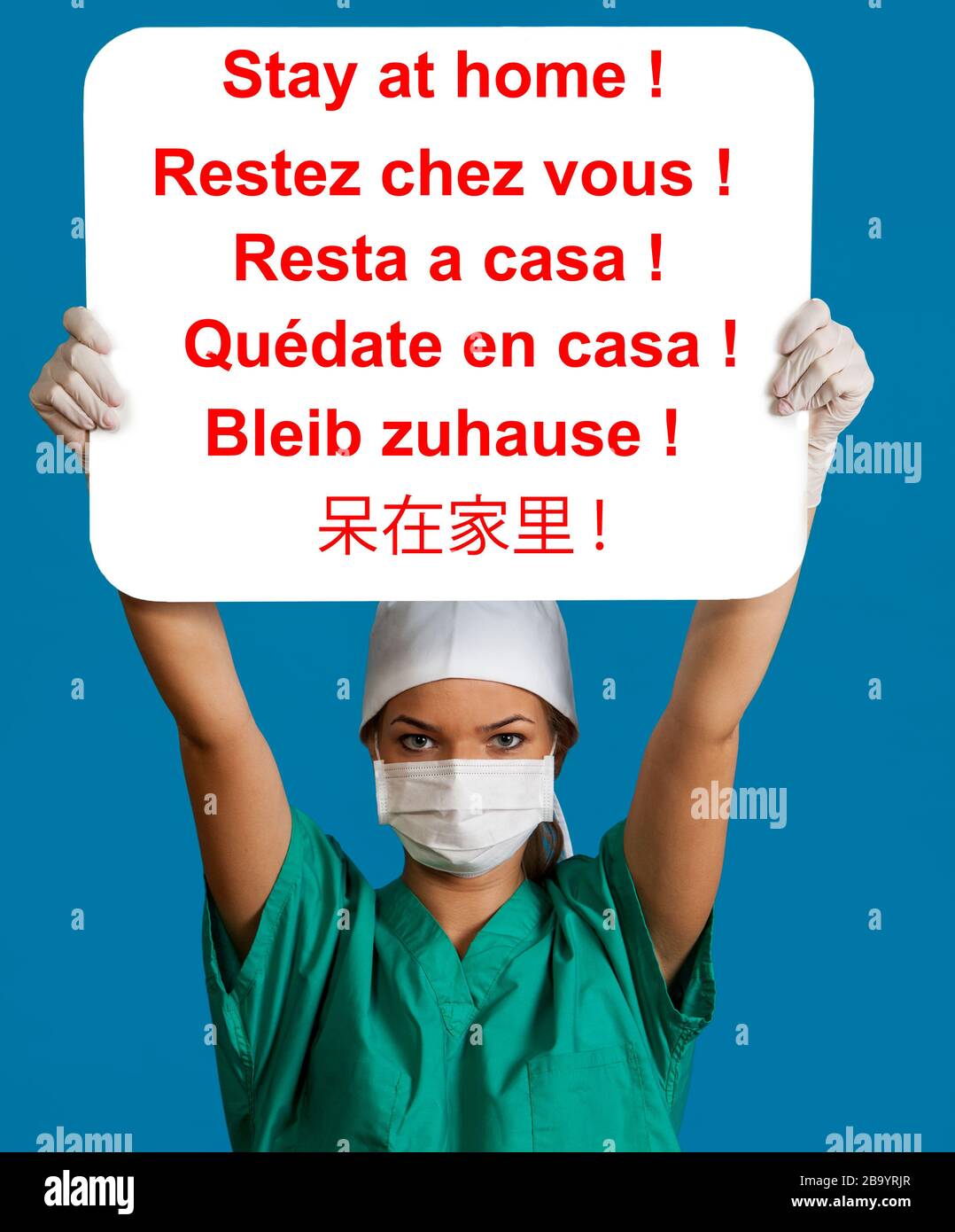 Una giovane infermiera in una maschera che tiene un pannello bianco sopra la sua testa con il messaggio di sei lingue rimanere a casa. Questo messaggio diventa lo svezzamento più importante Foto Stock