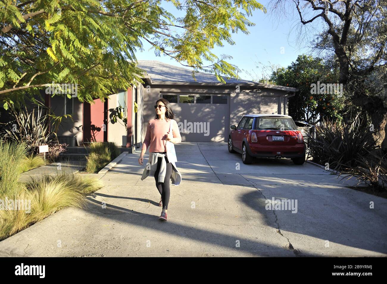 Donna asiatica che indossa un pullover rosa che cammina lungo un vialetto con una borsa tote intorno alle spalle. Foto Stock
