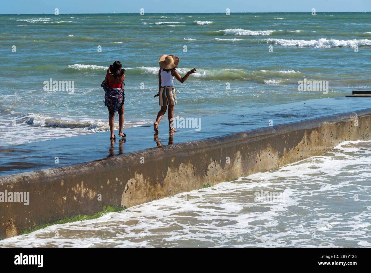 Strand, Somerset West, western cape, Sud Africa. Dic 2019. Giovani ragazze che si divertono a camminare lungo il muro di mare a Strand, Somerset West, Sud Africa Foto Stock