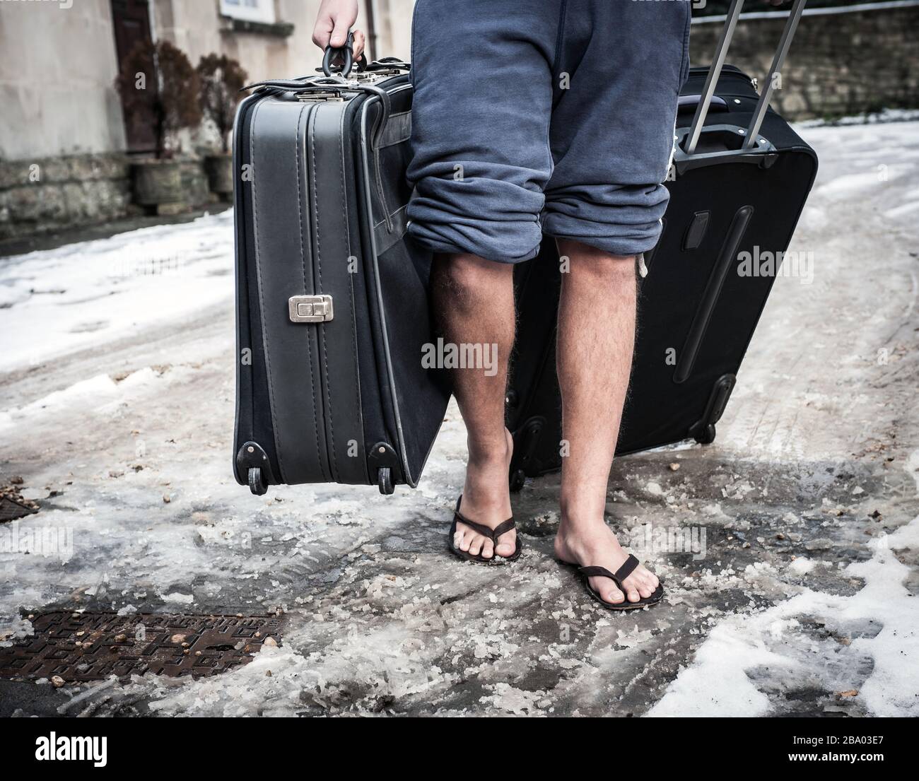 Uomo che cammina con valigia con infradito nella neve invernale Foto Stock