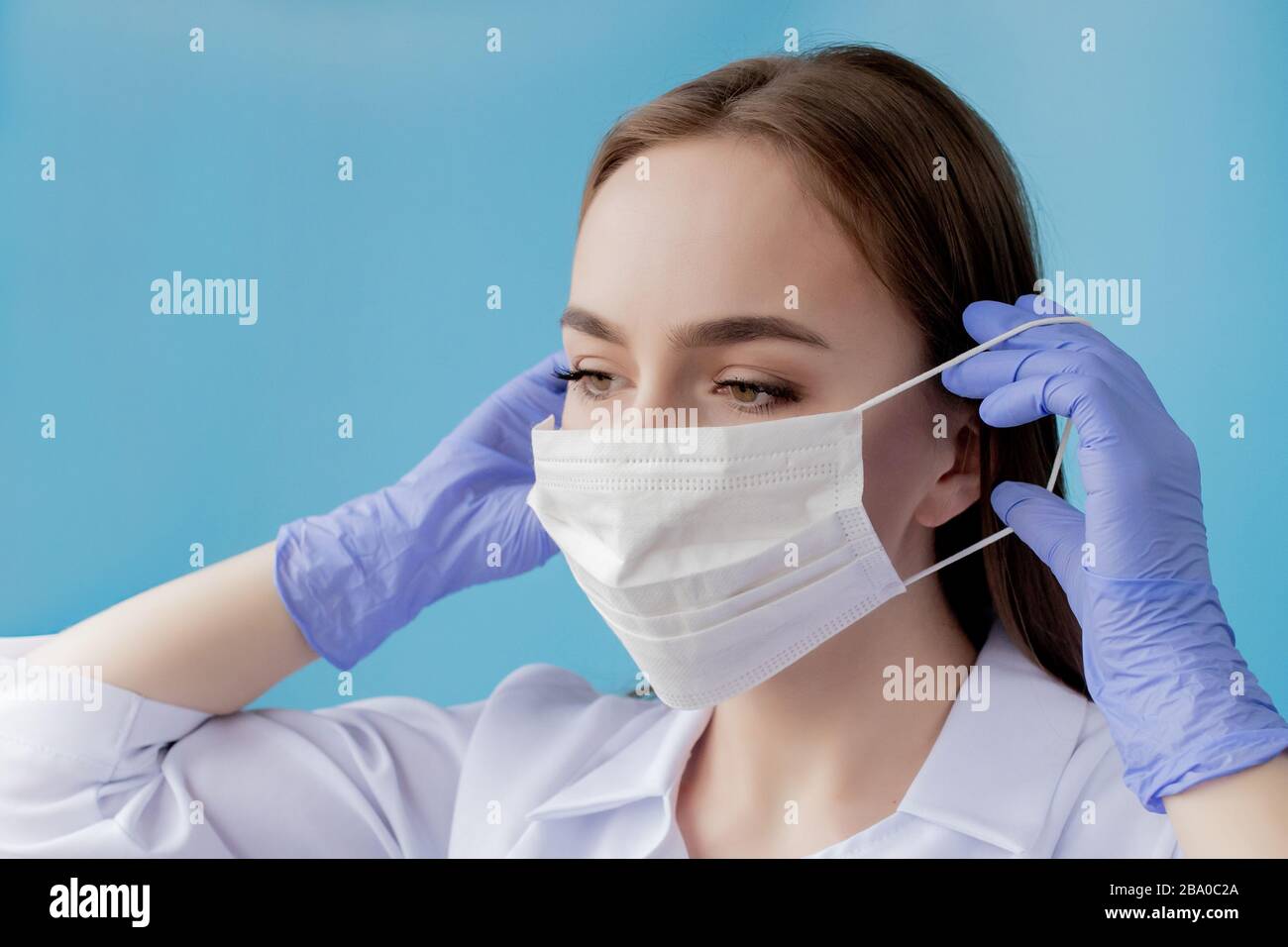 Infermiere medico sorridente dietro maschera chirurgo. Primo piano ritratto di giovane donna caucasica modello su sfondo blu. Donna che indossa la massa per proteggere covid-19 Foto Stock
