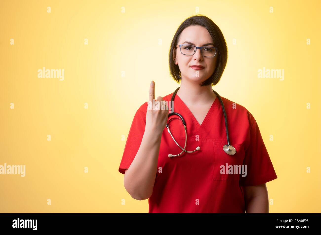 Ritratto di bella donna medico con stetoscopio con scrub rosa, contando uno con il suo dito in posa su uno sfondo isolato giallo. Foto Stock