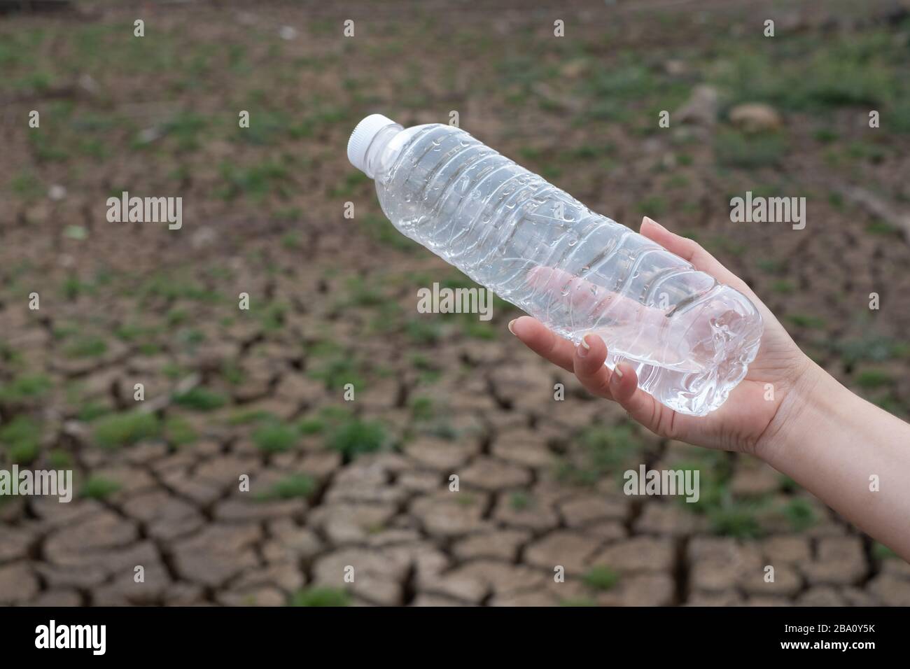 Primo piano donna mano tenendo la bottiglia di plastica trasparente a sfondo di terra crepa, questi rifiuti provengono da aree urbane e industriali non può sbarazzarsi di Foto Stock
