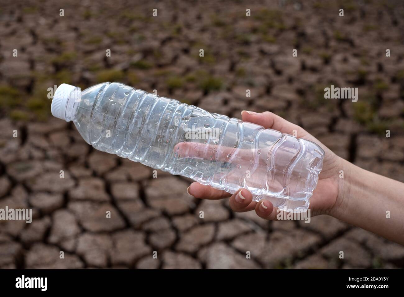 Primo piano donna mano tenendo la bottiglia di plastica trasparente a sfondo di terra crepa, questi rifiuti provengono da aree urbane e industriali non può sbarazzarsi di Foto Stock