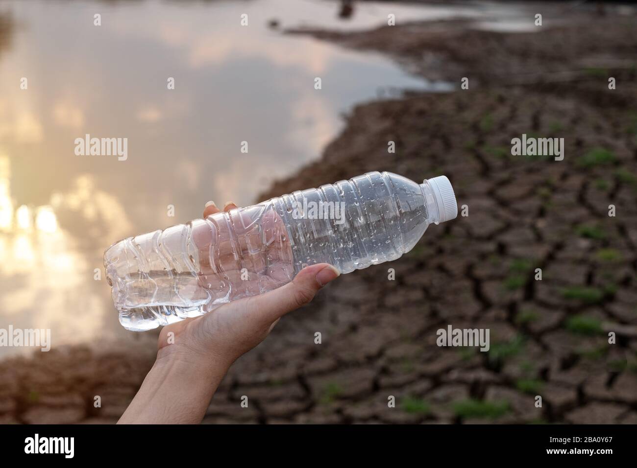 Primo piano donna mano tenendo la bottiglia di plastica trasparente a sfondo di terra crepa, questi rifiuti provengono da aree urbane e industriali non può sbarazzarsi di Foto Stock