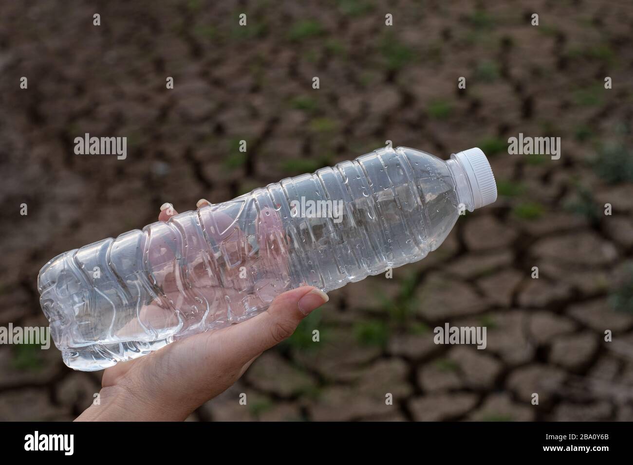 Primo piano donna mano tenendo la bottiglia di plastica trasparente a sfondo di terra crepa, questi rifiuti provengono da aree urbane e industriali non può sbarazzarsi di Foto Stock