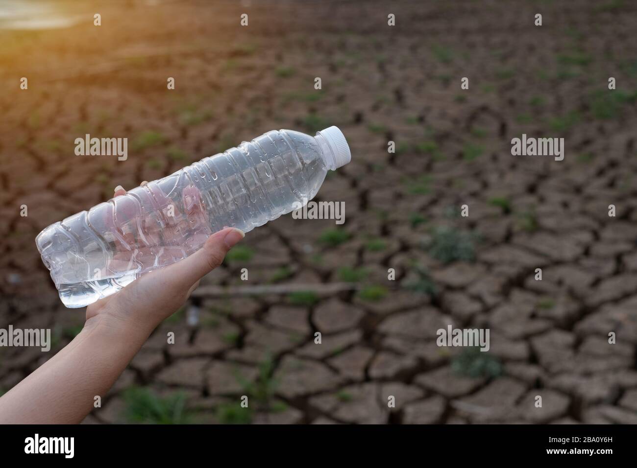 Primo piano donna mano tenendo la bottiglia di plastica trasparente a sfondo di terra crepa, questi rifiuti provengono da aree urbane e industriali non può sbarazzarsi di Foto Stock