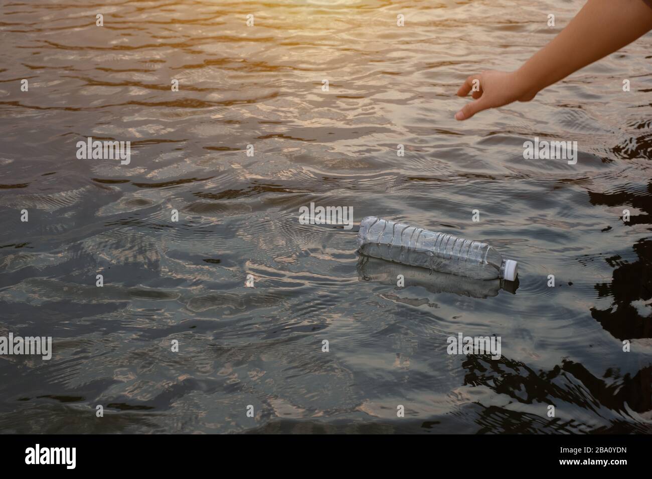 Mano della donna per raccogliere la bottiglia di plastica di scarto usata sull'acqua in un canale Foto Stock