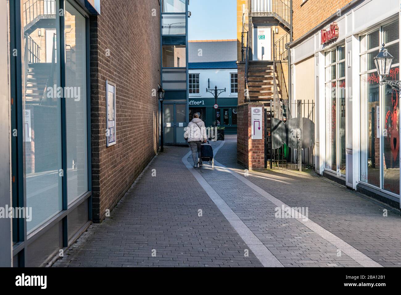 Marzo 2020. Una donna cammina lungo un vicolo deserto nel centro della città, a metà settimana nel pomeriggio durante la chiusura inglese. Bicester, Oxfordshire, Regno Unito Foto Stock