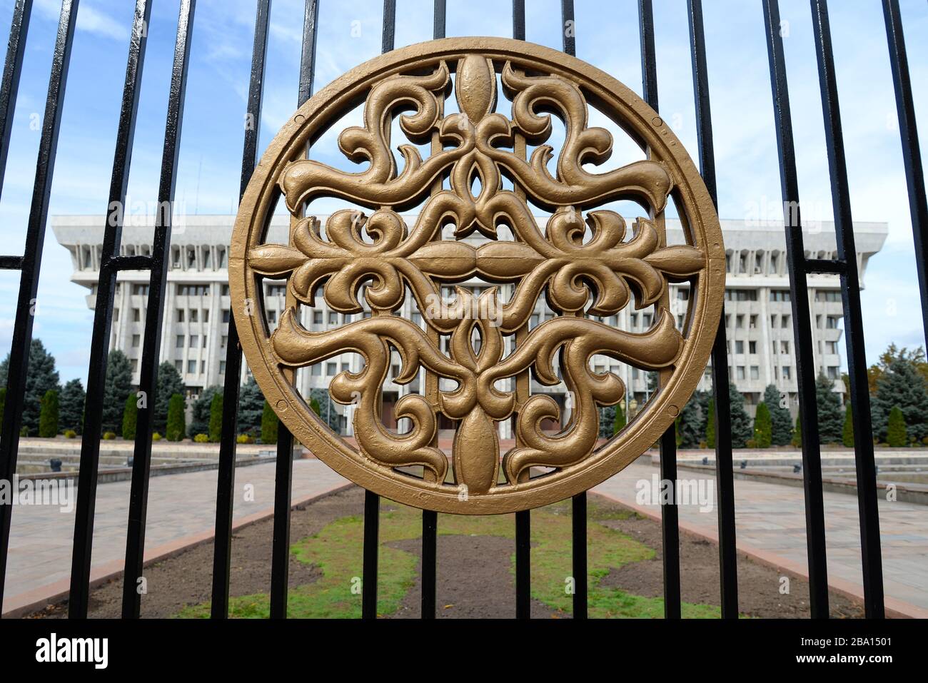 Simbolo di metallo giallo in una recinzione di fronte alla Casa Bianca di Bishkek, il parlamento di governo in stile architettonico stalinista in Kirghizistan. Foto Stock