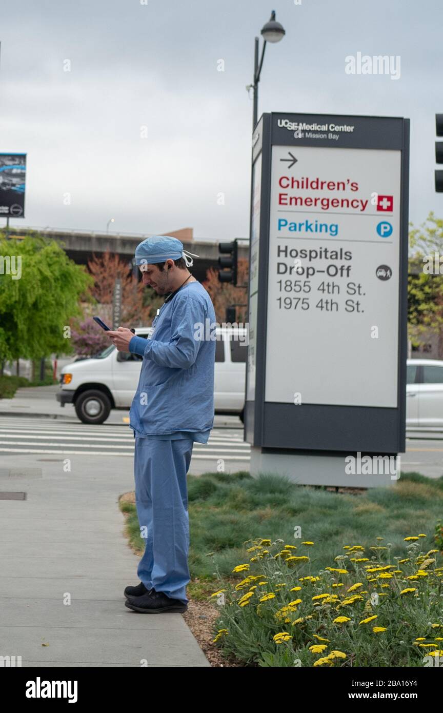 Un fornitore medico in scrub si trova vicino ad un cartello al di fuori del centro medico della University of California San Francisco (UCSF) a Mission Bay durante uno scoppio del coronavirus COVID-19 a San Francisco, California, 23 marzo 2020. () Foto Stock