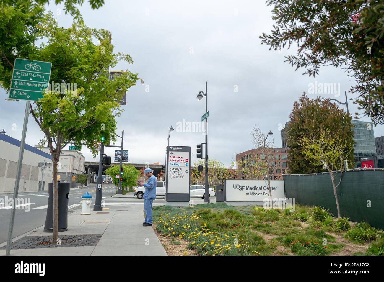 Un fornitore medico in scrub si trova vicino ad un cartello al di fuori del centro medico della University of California San Francisco (UCSF) a Mission Bay durante uno scoppio del coronavirus COVID-19 a San Francisco, California, 23 marzo 2020. () Foto Stock