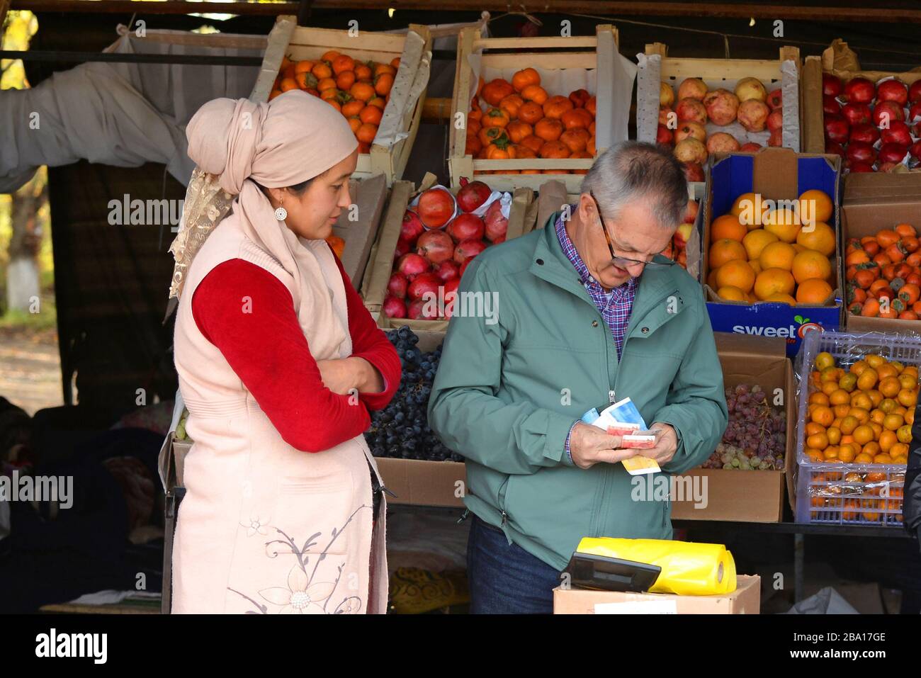 Venditore locale che vende frutta e verdura fresca in un mercato in stallo sulla strada Bishkek, Kirghizistan. Turista scegliere la fattura/banconota locale corretta. Foto Stock