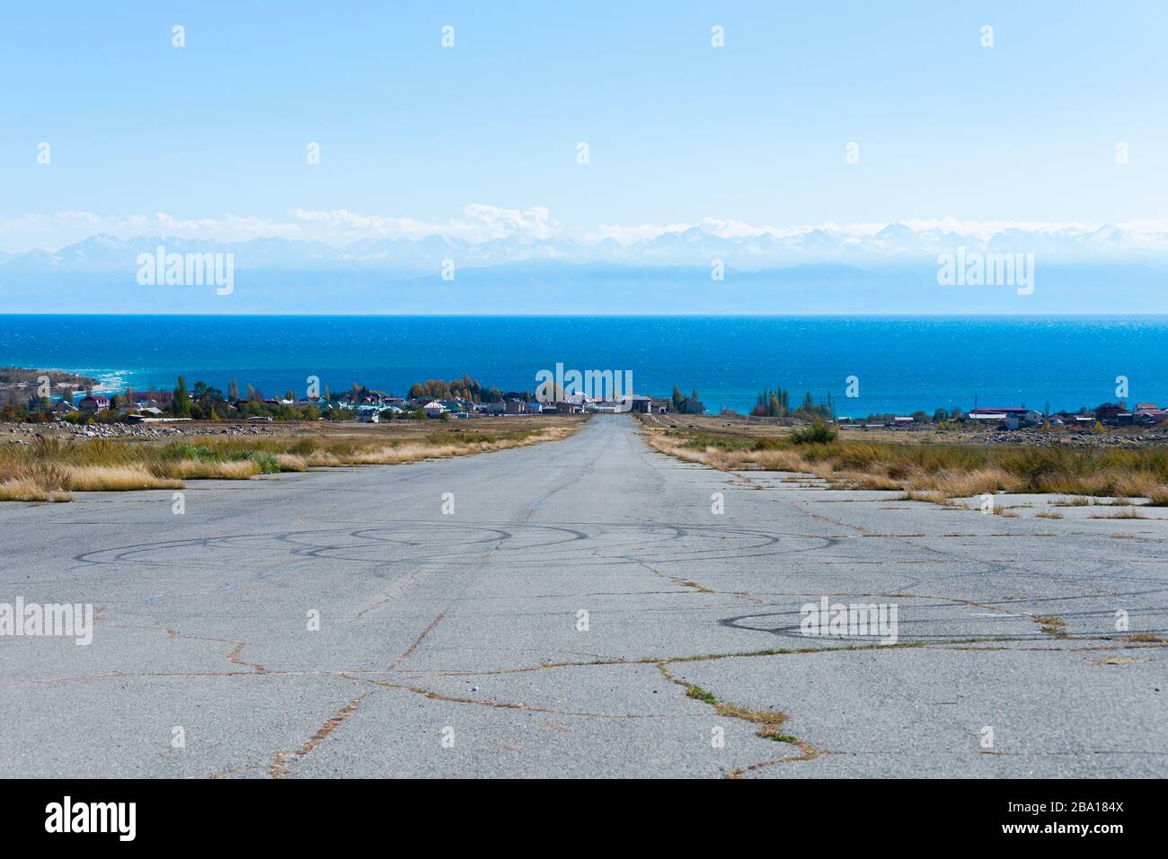 Aeroporto abbandonato pista asfaltata vicino Issyk Kul Lago in Kirghizistan. Vista dalla pista dell'airfield che guarda al lago alpino con montagne innevate. Foto Stock